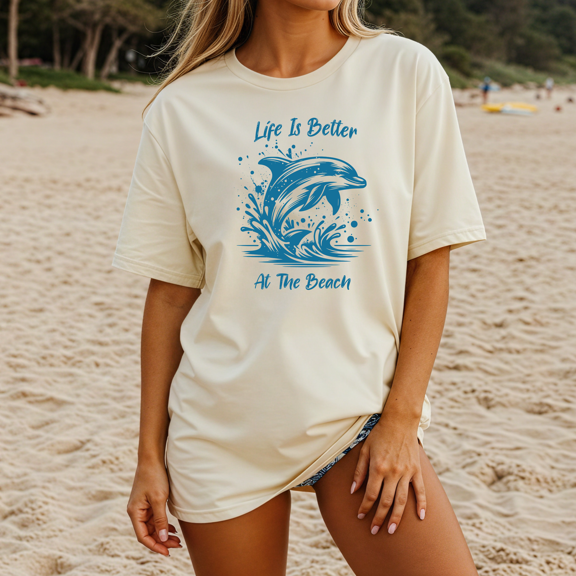 Comfort Colors 1717 "Life is Better at the Beach" t shirt with a dolphin jumping out of the water in one color graphic. Picture of a girl on the beach in an oversized t shirt.