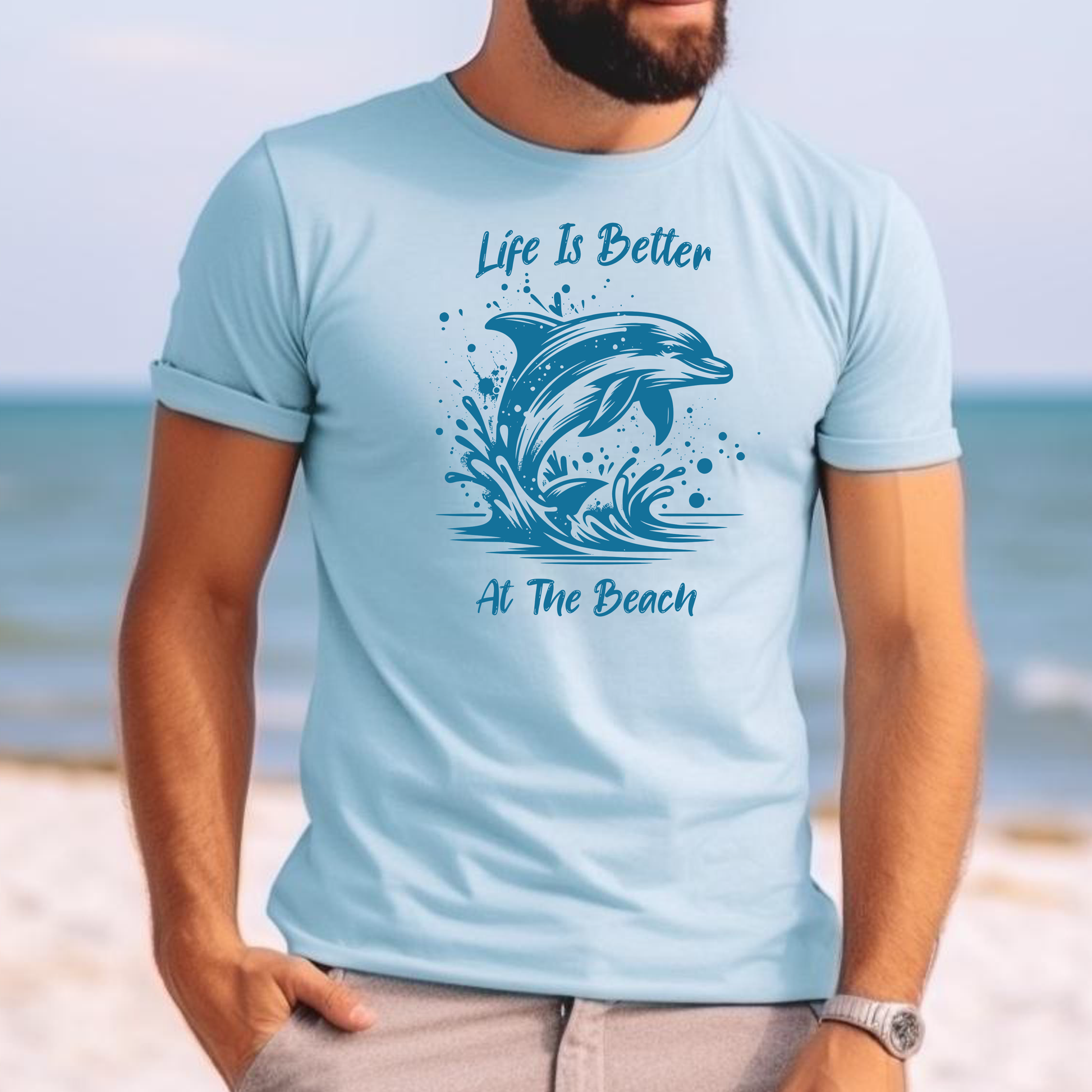 Comfort Colors 1717 "Life is Better at the Beach" t shirt with a dolphin jumping out of the water in one color graphic. Picture of a man on the beach in a t shirt.