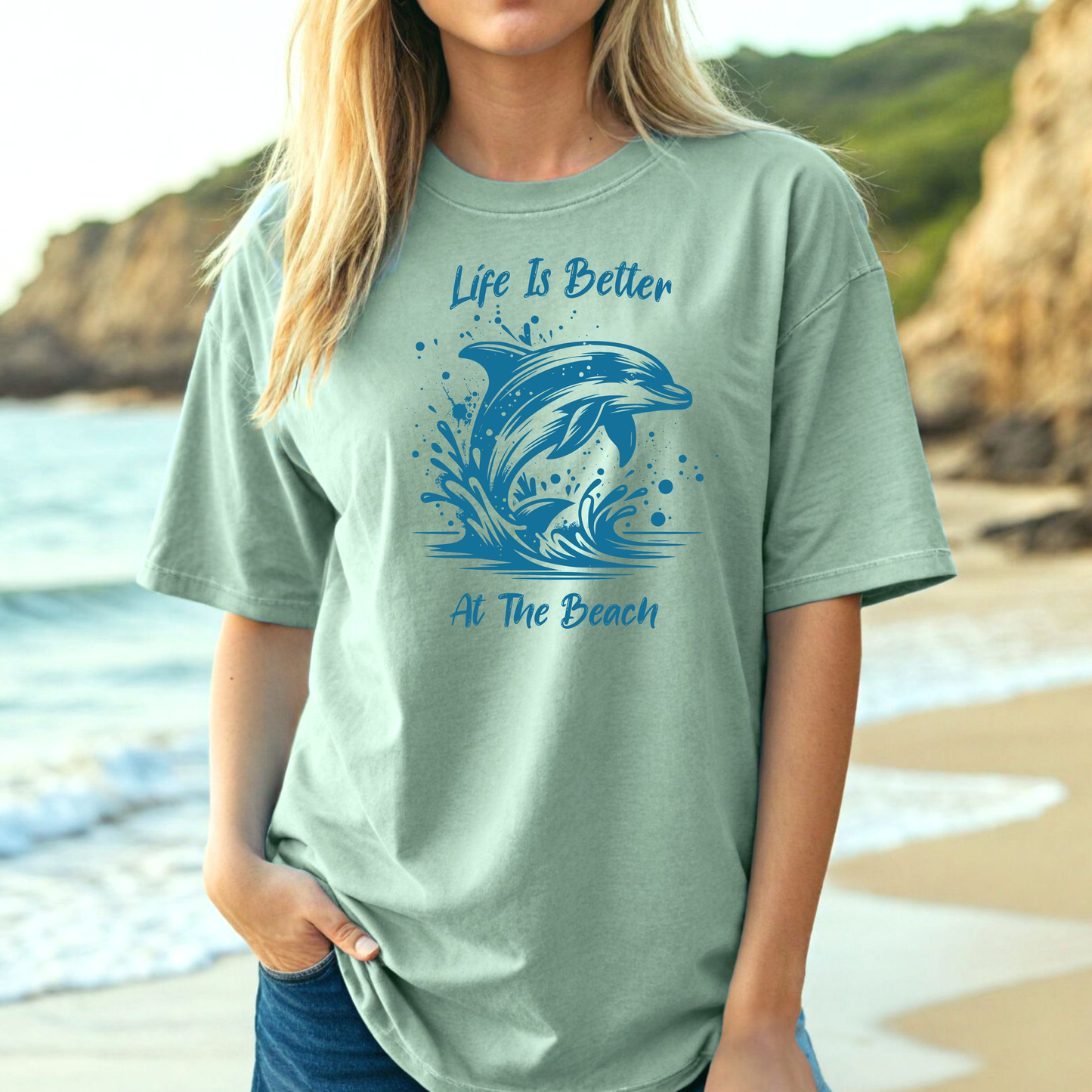 Comfort Colors 1717 "Life is Better at the Beach" t shirt with a dolphin jumping out of the water in one color graphic. Picture of a girl on the beach in an oversized t shirt.