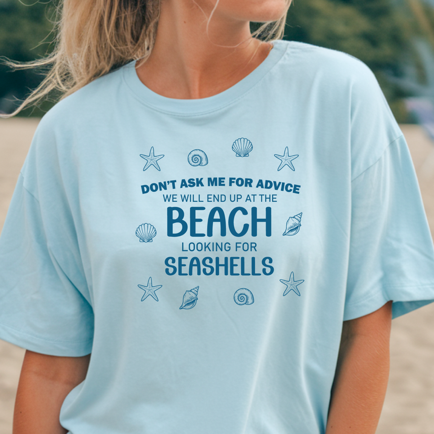 Light blue t-shirt with beach-themed text and graphics worn by a person.