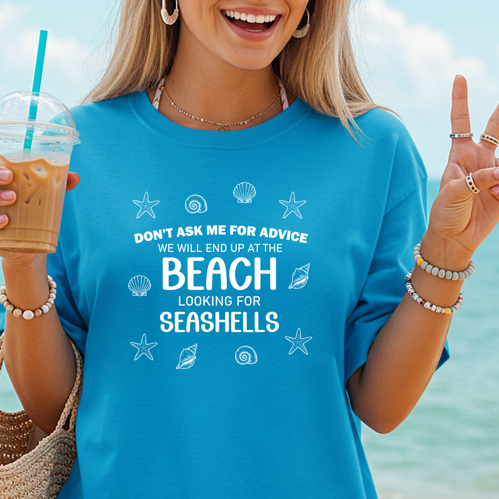 Woman wearing a blue t-shirt with beach-themed text and graphics, holding a drink with a straw.