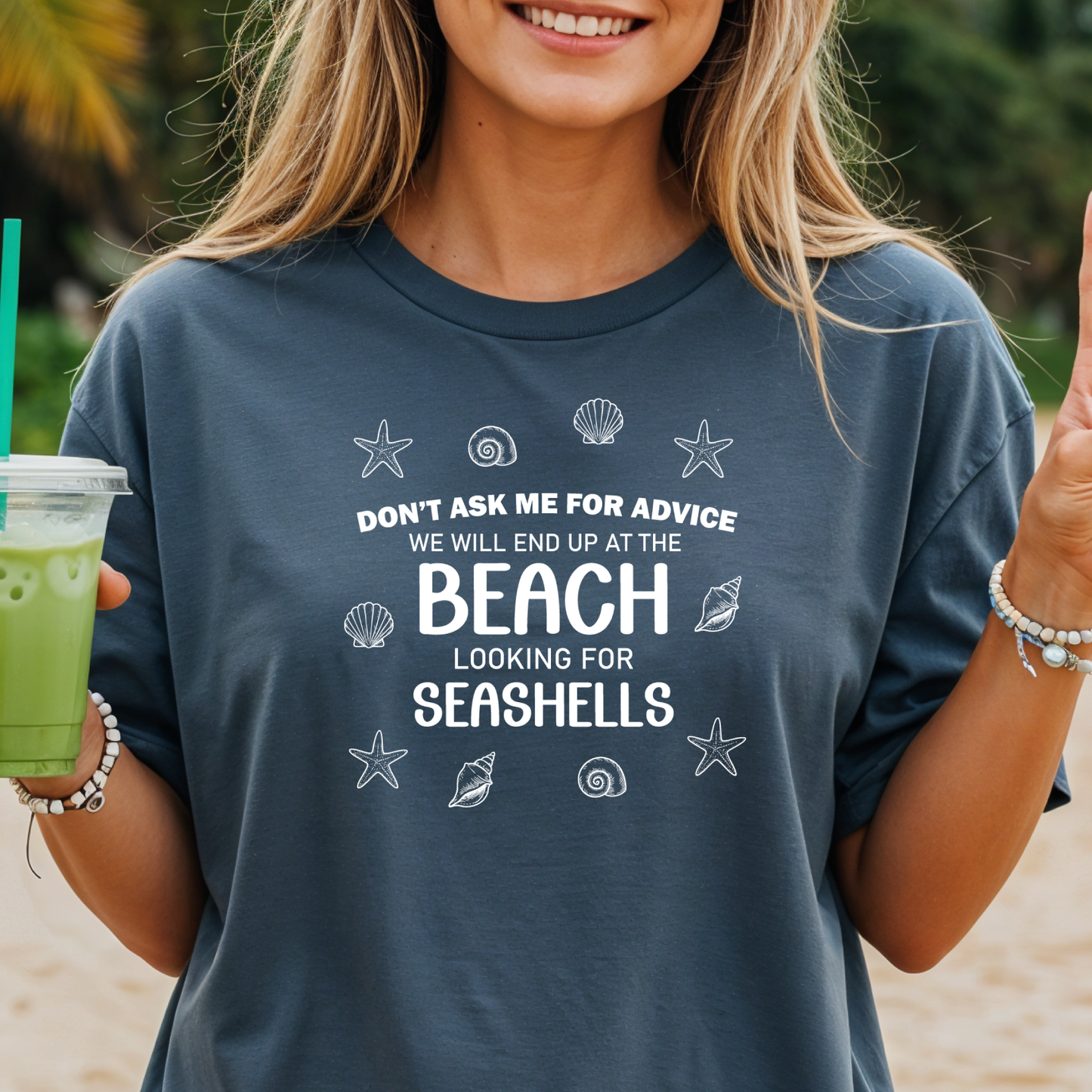 Person wearing a t-shirt with a beach-themed quote, holding a drink on a beach.