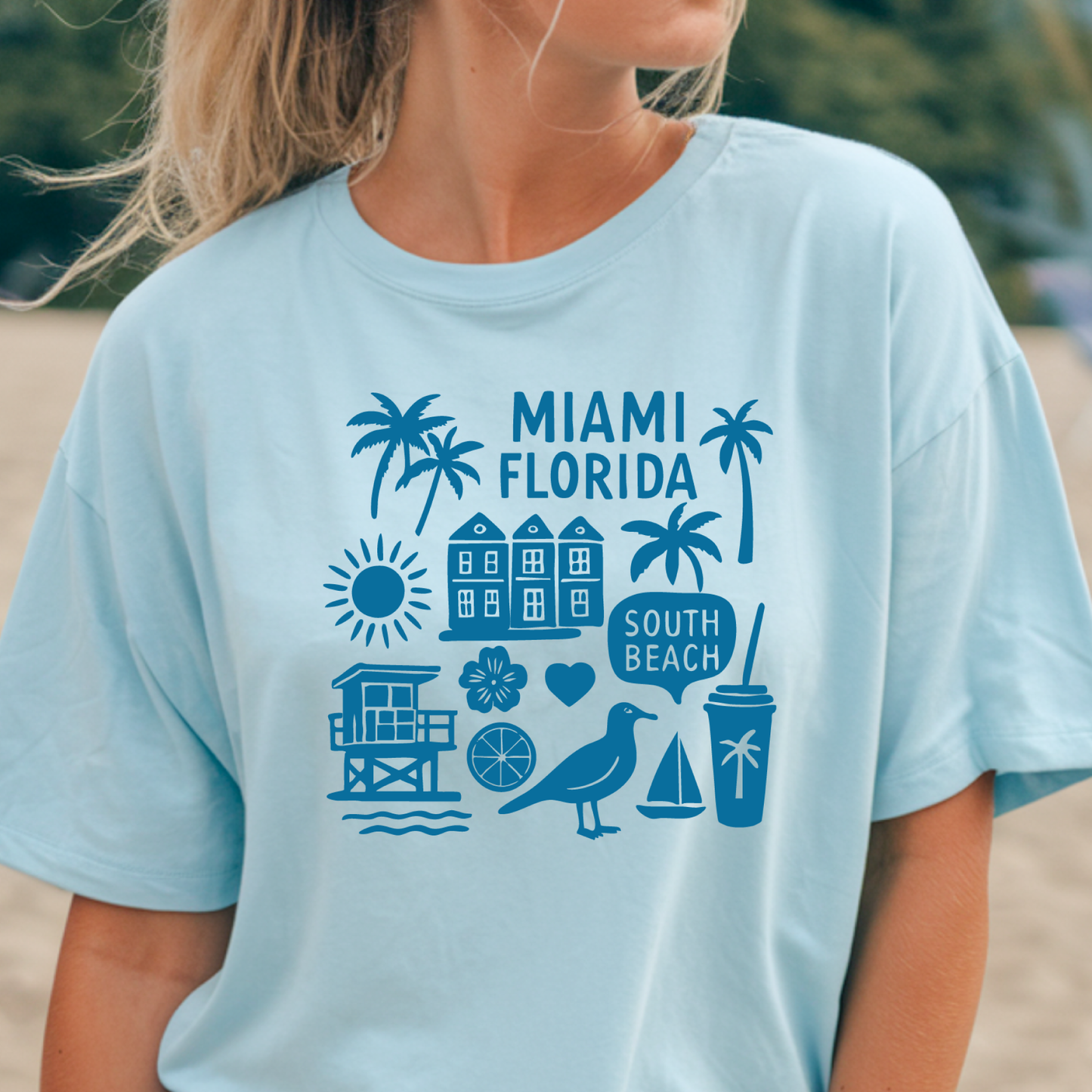 Light blue t-shirt with blue graphics and text 'Miami Florida' worn by a person on a beach.