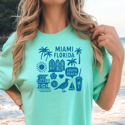 Person wearing a green t-shirt with 'Miami Florida' and beach icons on a beach background