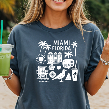 Person wearing a navy blue t-shirt with 'Miami Florida' and beach icons, holding a green drink.