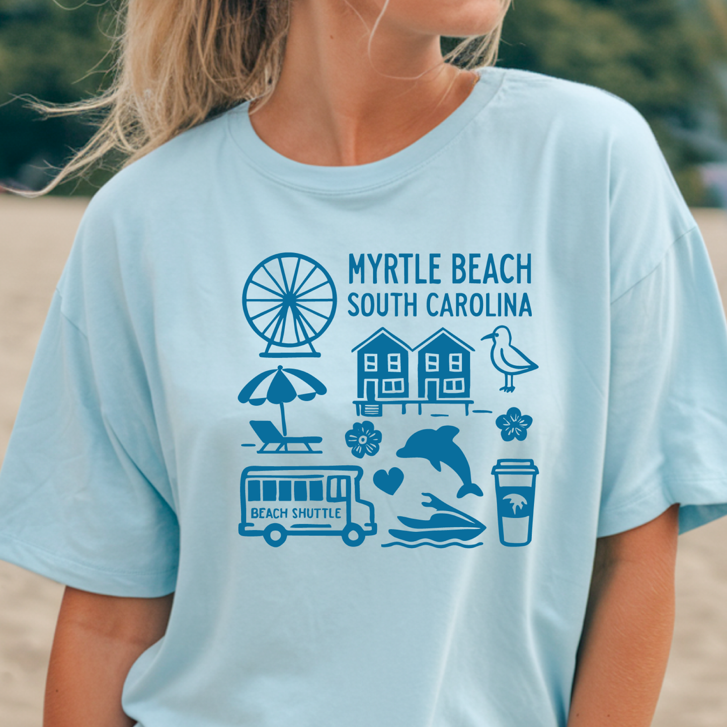 Light blue t-shirt with blue graphics and text on a beach setting