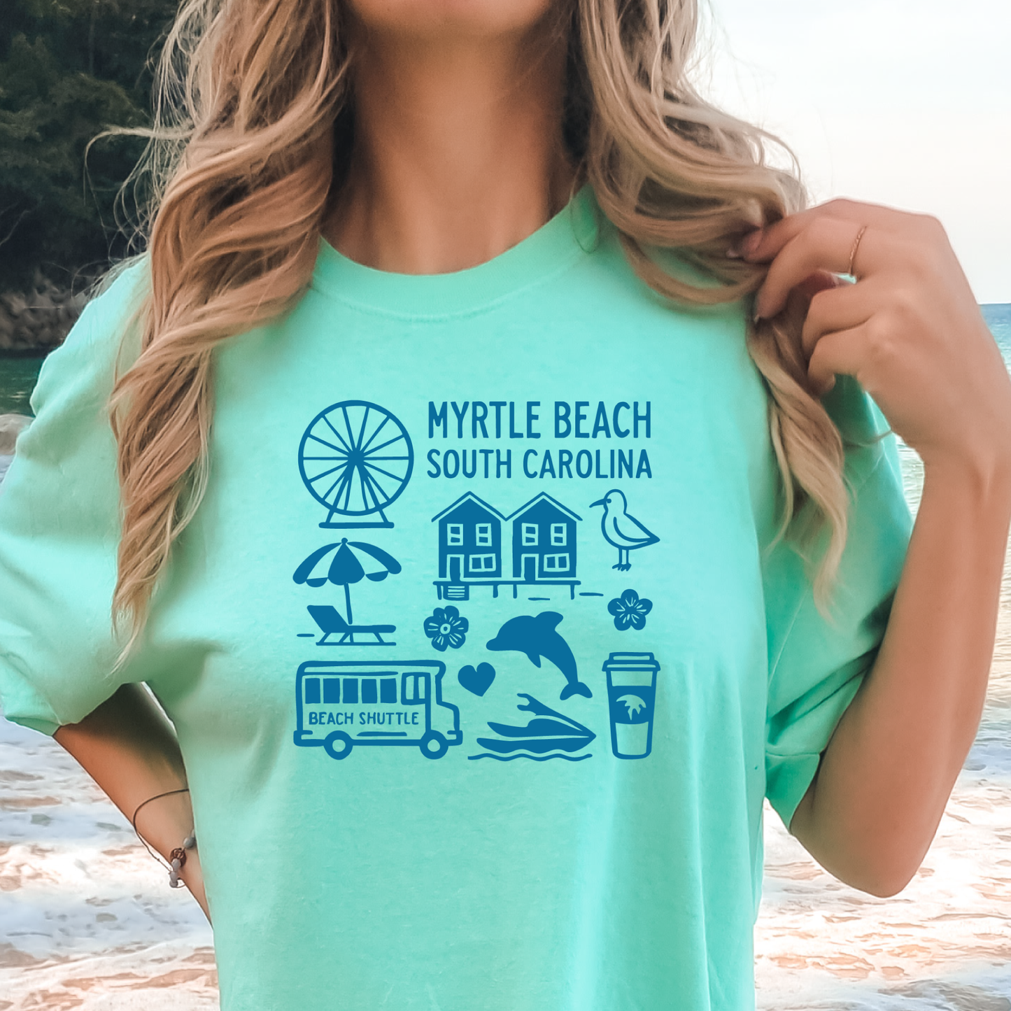 Person wearing a light green t-shirt with 'Myrtle Beach South Carolina' graphics on a beach.