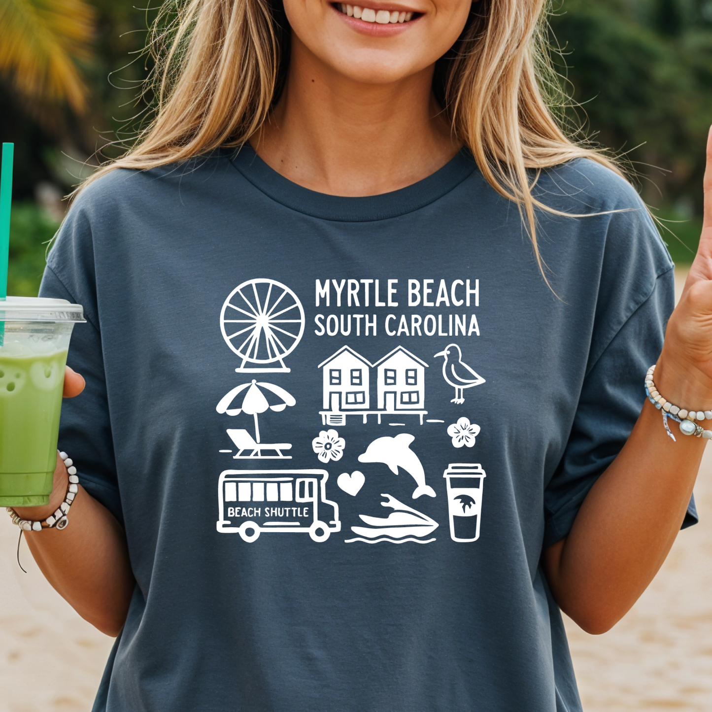 Person wearing a navy t-shirt with 'Myrtle Beach South Carolina' design, holding a green drink.