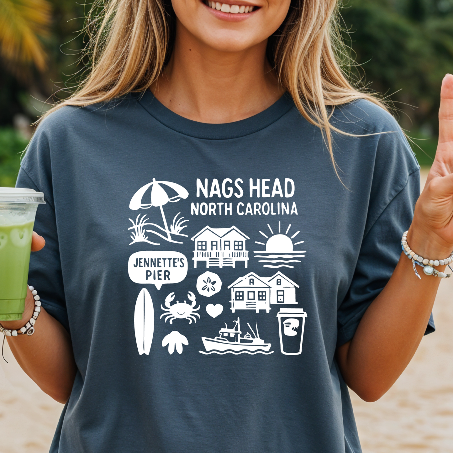 Person wearing a blue t-shirt with Nags Head, North Carolina graphics on a beach.