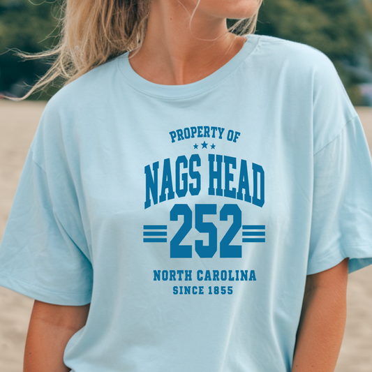 Light blue t-shirt with 'Property of Nags Head 252 North Carolina Since 1855' text worn by a person.