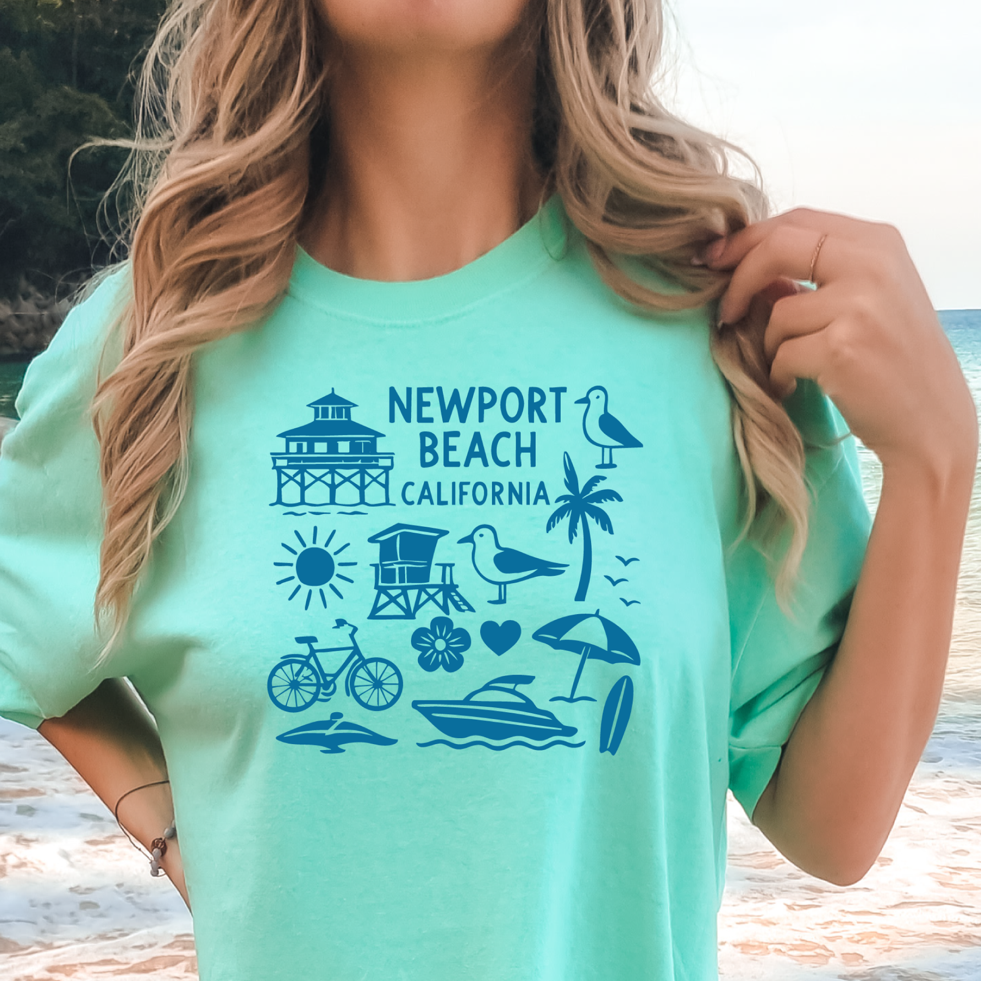 Person wearing a green t-shirt with Newport Beach California graphics on a beach.