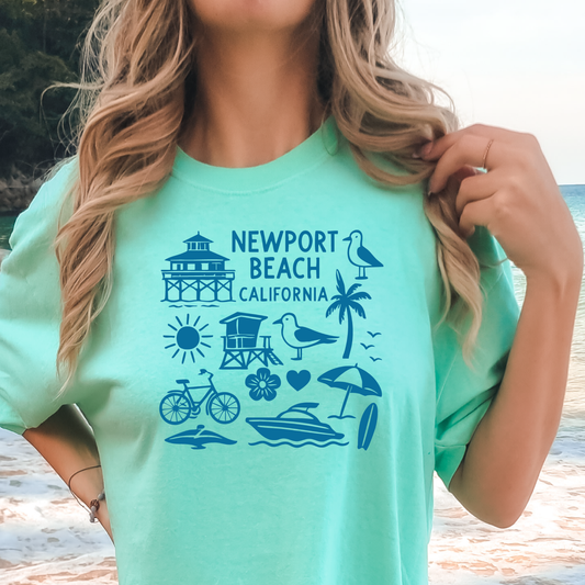 Person wearing a green t-shirt with Newport Beach California graphics on a beach.