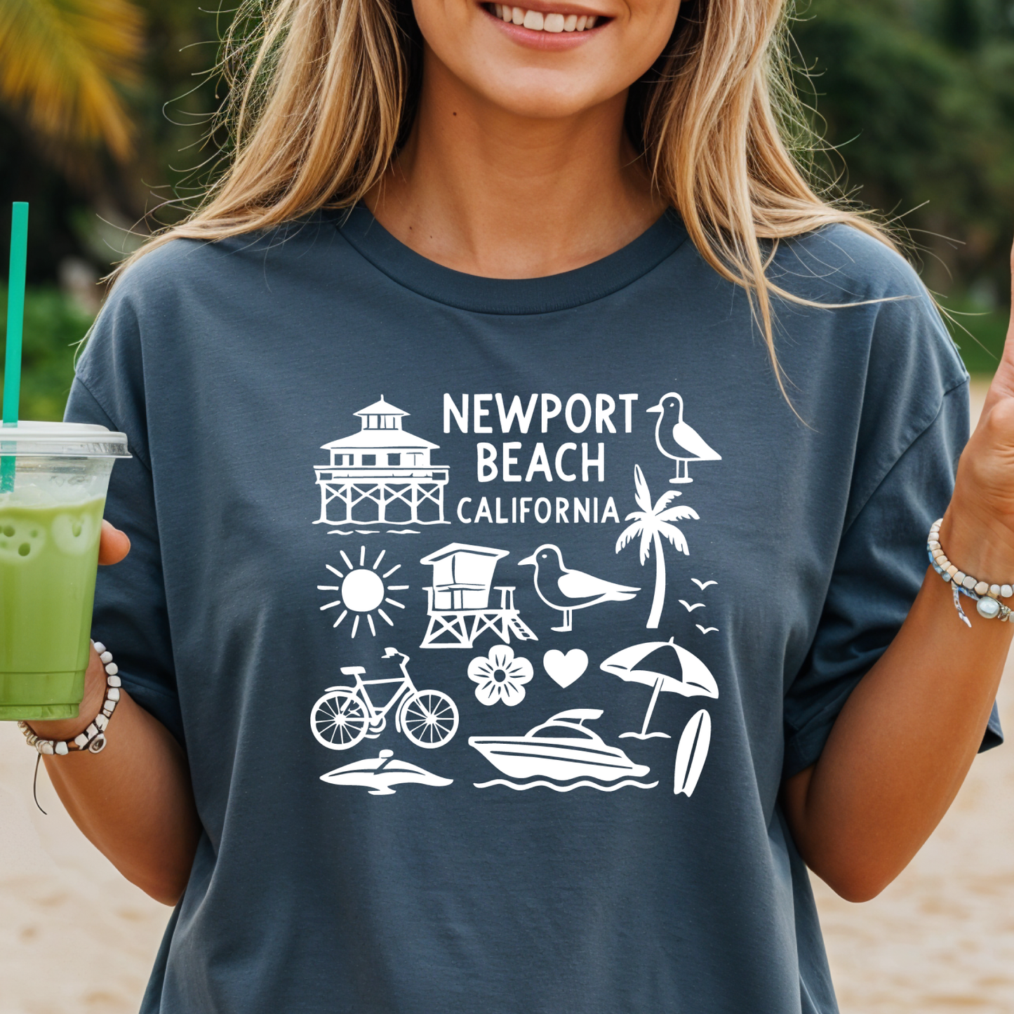 Person wearing a navy t-shirt with 'Newport Beach California' design, holding a green drink.