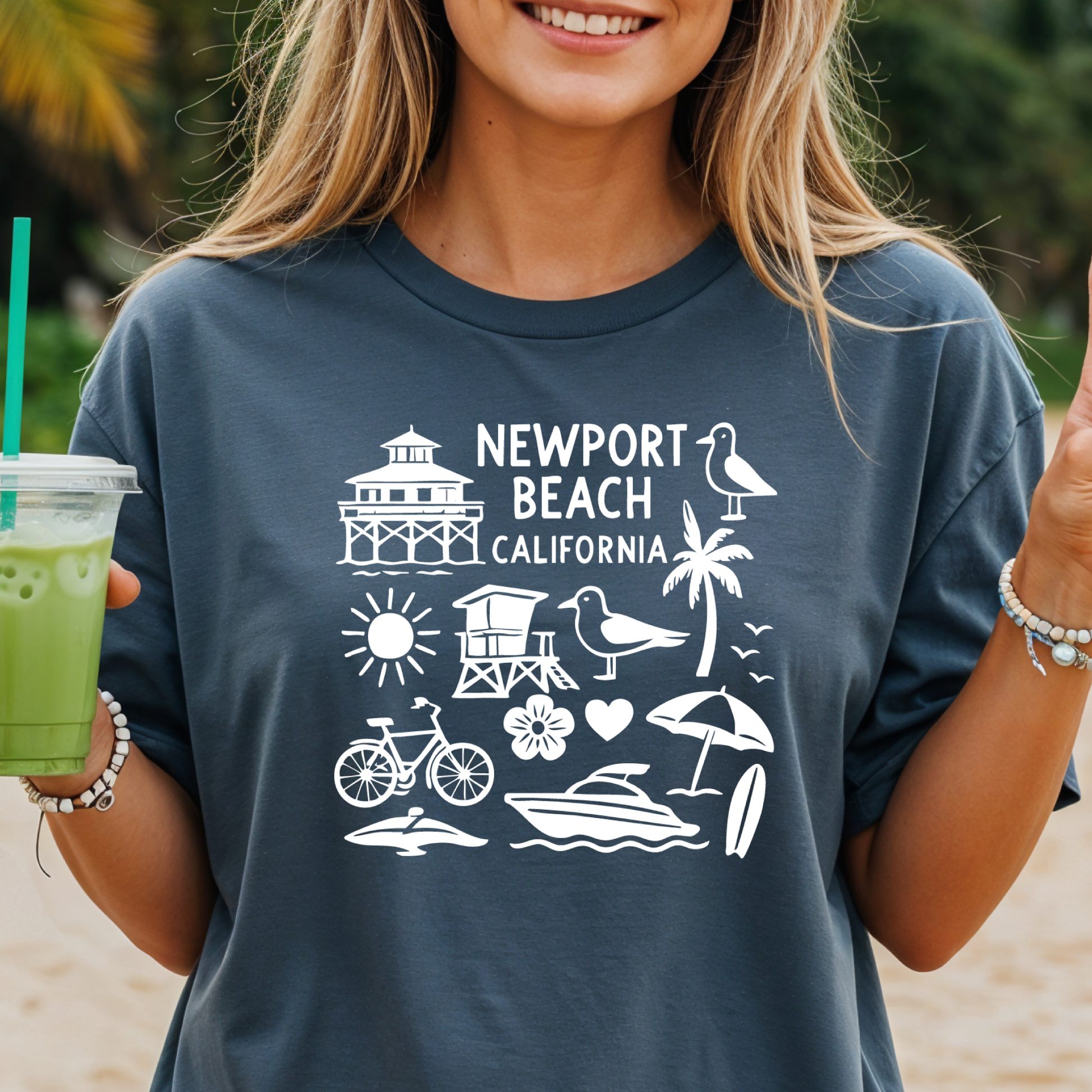 Person wearing a navy t-shirt with 'Newport Beach California' design, holding a green drink.