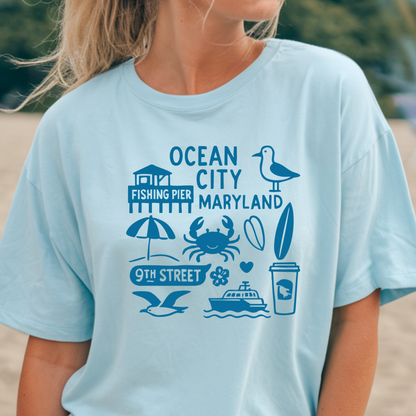 Light blue t-shirt with Ocean City, Maryland graphics worn by a person on a beach.