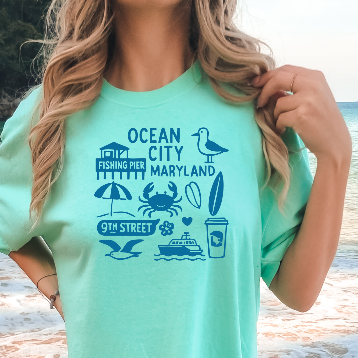 Person wearing a green t-shirt with Ocean City, Maryland graphics on a beach.
