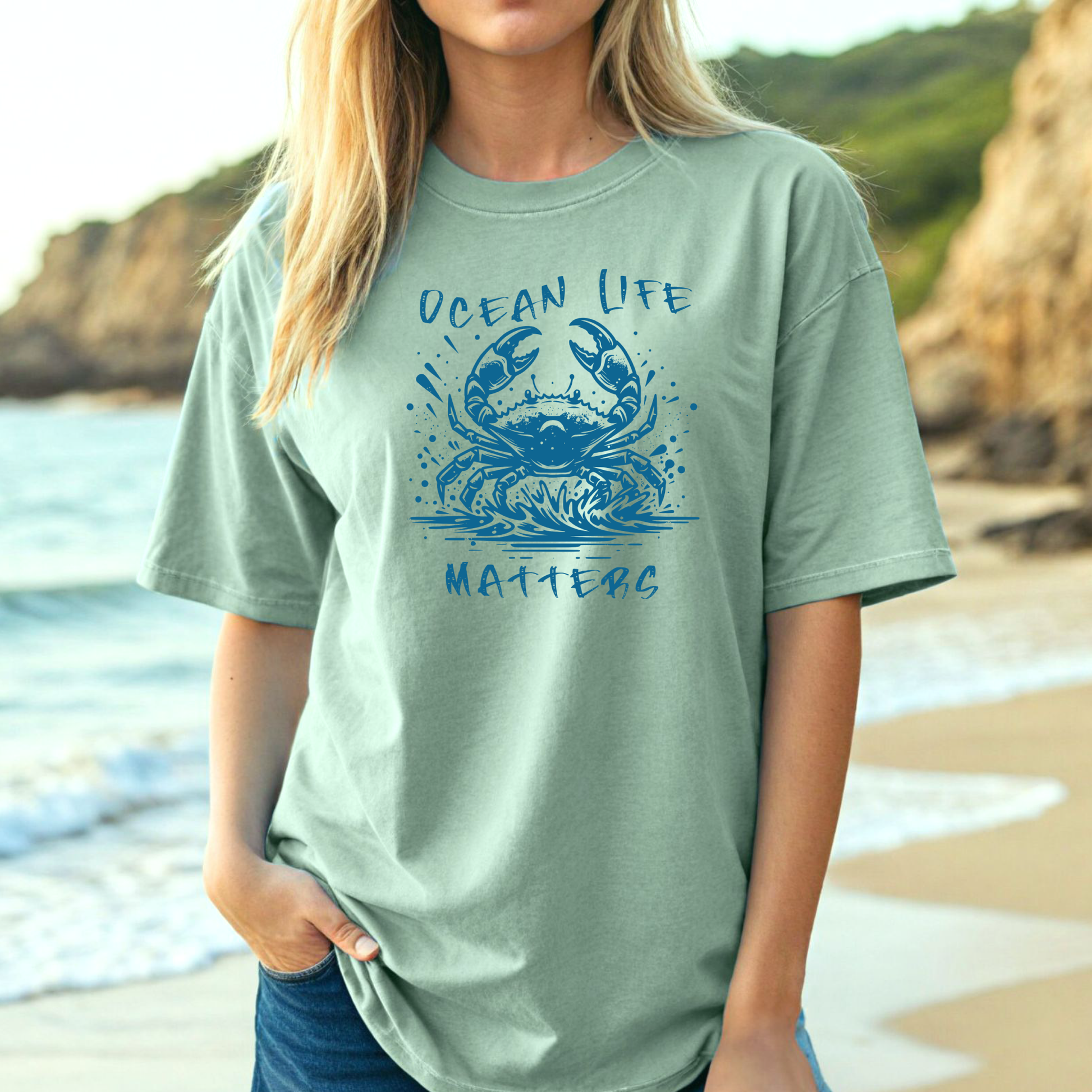Comfort Colors 1717 "Ocean Life Matters" t shirt with a crab splashing in water in a one color graphic. Picture of a girl standing on the beach wearing an oversized t shirt.