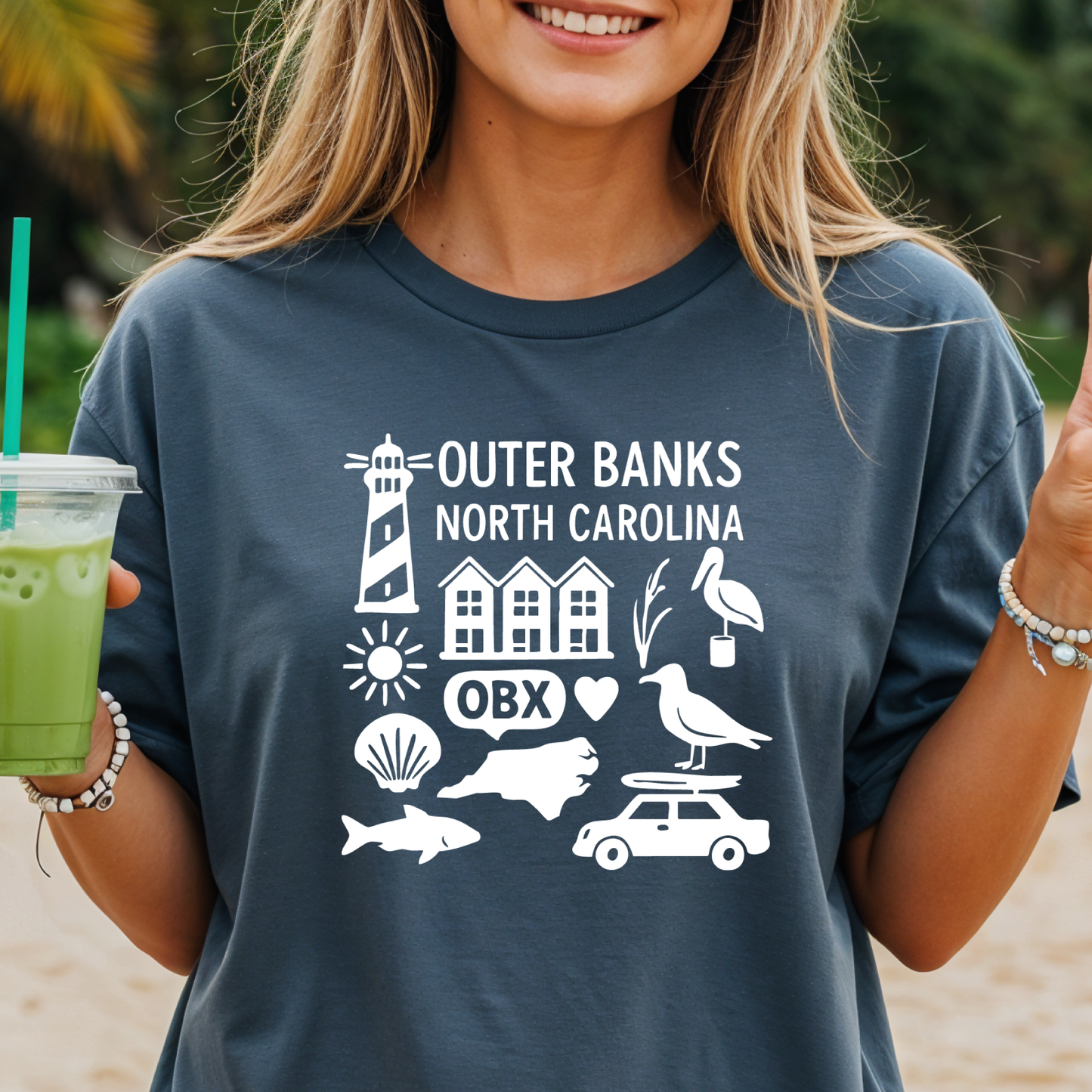 Person wearing a navy t-shirt with Outer Banks, North Carolina graphics on a beach.