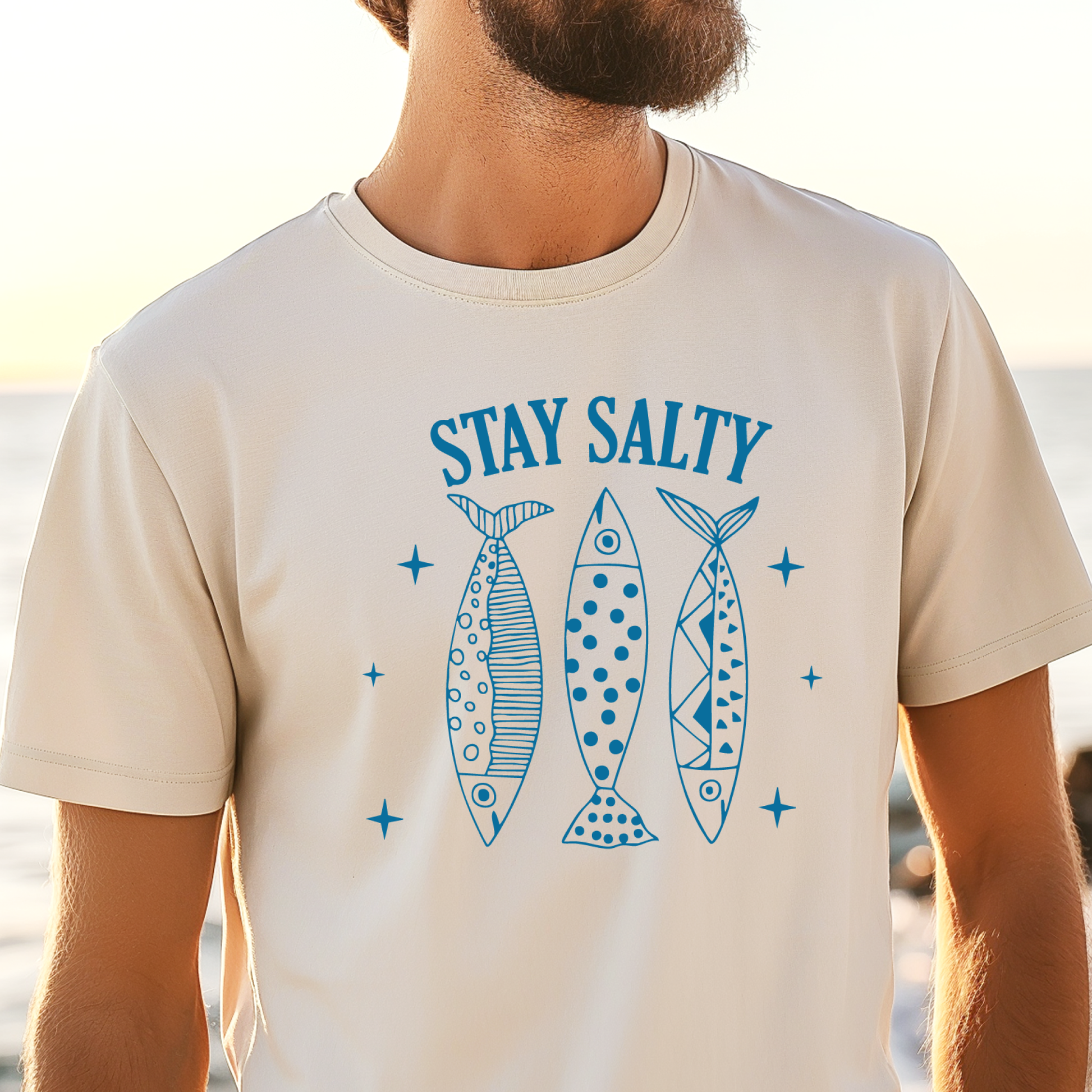 Person wearing a t-shirt with 'Stay Salty' and fish graphics at the beach.