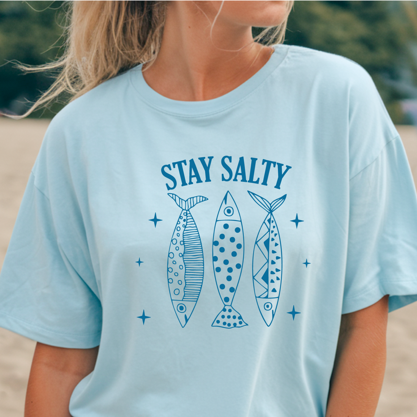 Person wearing a light blue t-shirt with 'Stay Salty' text and fish illustrations.