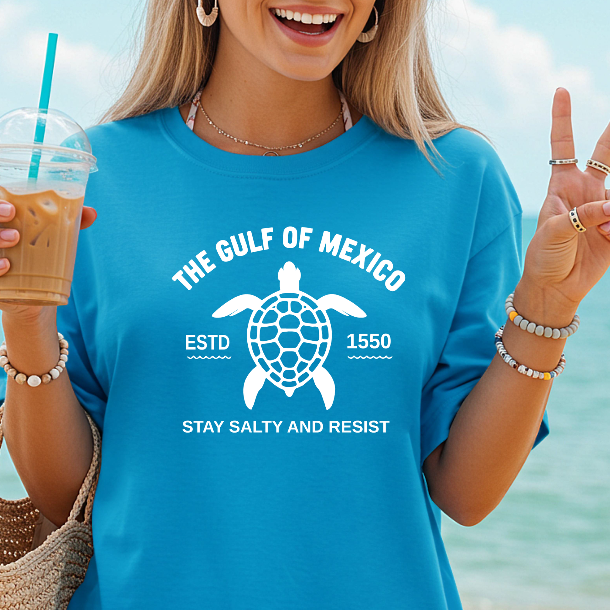 Person wearing a blue t-shirt with a turtle graphic and text by the beach