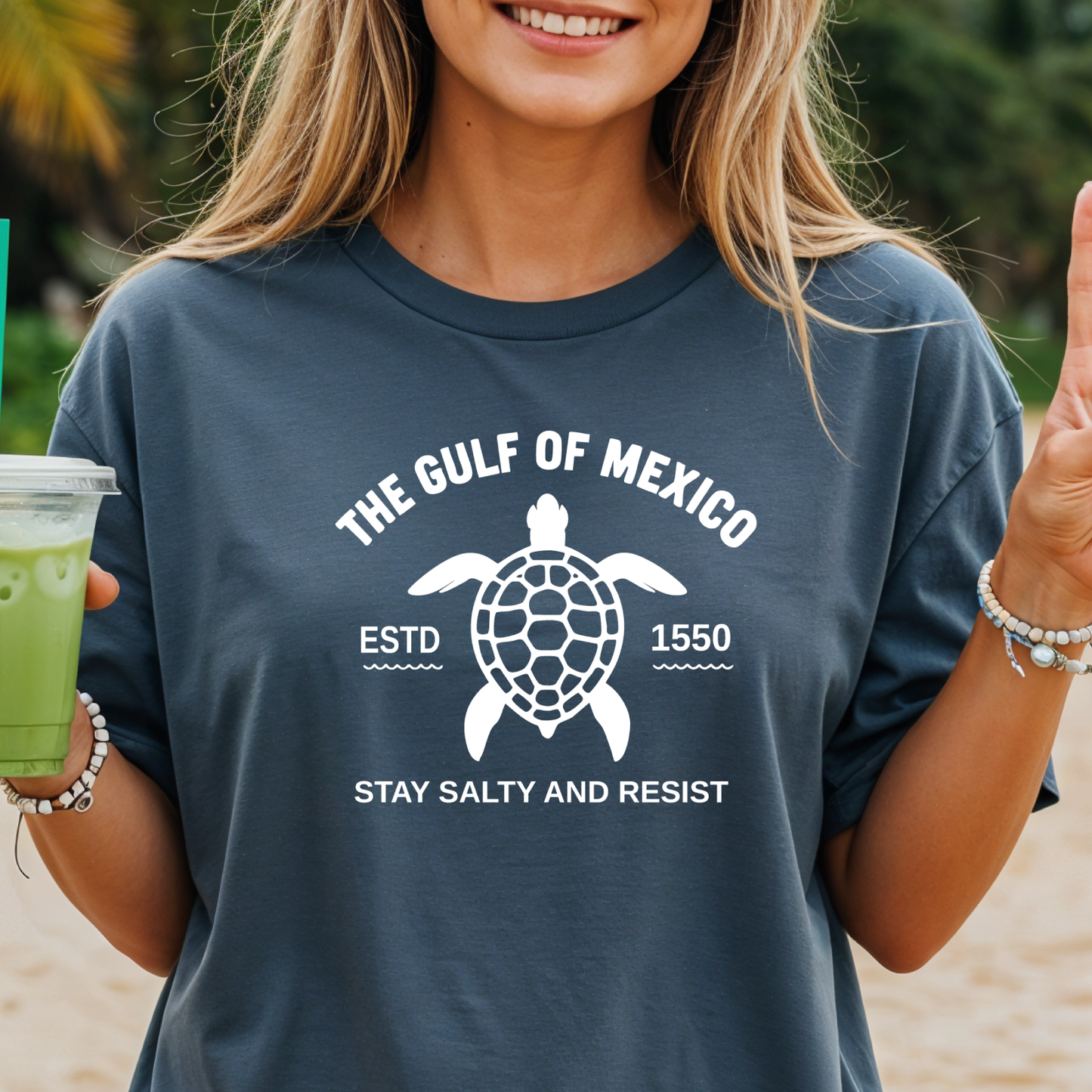 Person wearing a t-shirt with a turtle graphic and text on a beach