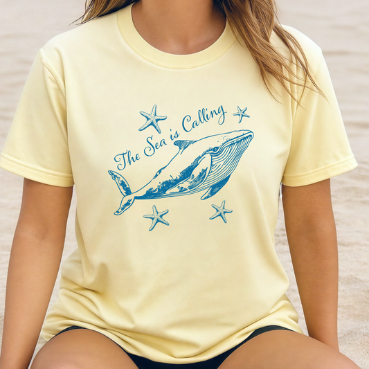 Comfort Colors t-shirt featuring a blue whale illustration surrounded by starfish and the handwritten-style text “The Sea is Calling.” The detailed marine artwork creates a calming coastal aesthetic. This unisex garment-dyed tee offers a soft vintage feel and relaxed fit, perfect for ocean lovers, beach trips, and anyone who enjoys sea-themed graphic shirts with a coastal vibe.