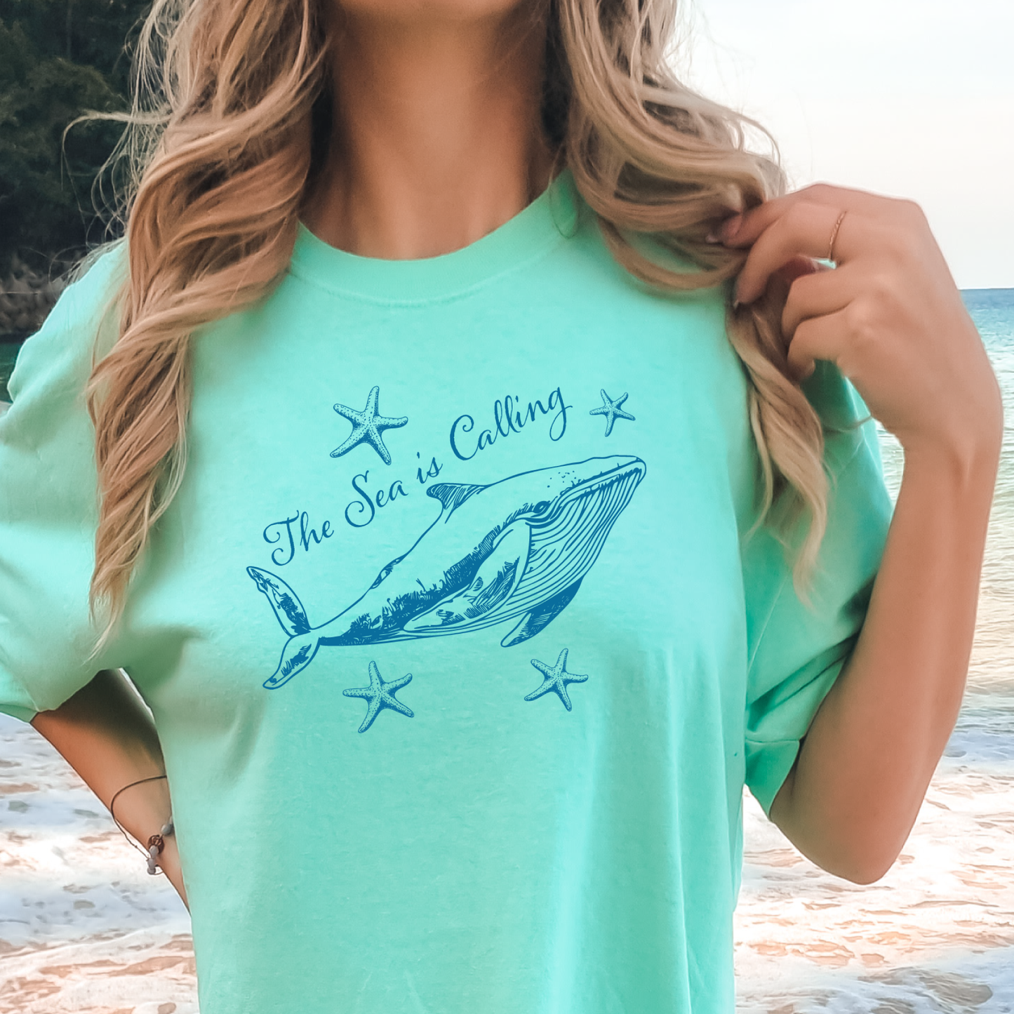 Comfort Colors t-shirt featuring a blue whale illustration surrounded by starfish and the handwritten-style text “The Sea is Calling.” The detailed marine artwork creates a calming coastal aesthetic. This unisex garment-dyed tee offers a soft vintage feel and relaxed fit, perfect for ocean lovers, beach trips, and anyone who enjoys sea-themed graphic shirts with a coastal vibe.