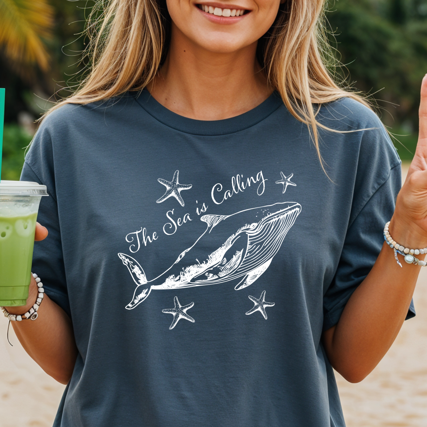 Comfort Colors t-shirt featuring a blue whale illustration surrounded by starfish and the handwritten-style text “The Sea is Calling.” The detailed marine artwork creates a calming coastal aesthetic. This unisex garment-dyed tee offers a soft vintage feel and relaxed fit, perfect for ocean lovers, beach trips, and anyone who enjoys sea-themed graphic shirts with a coastal vibe.