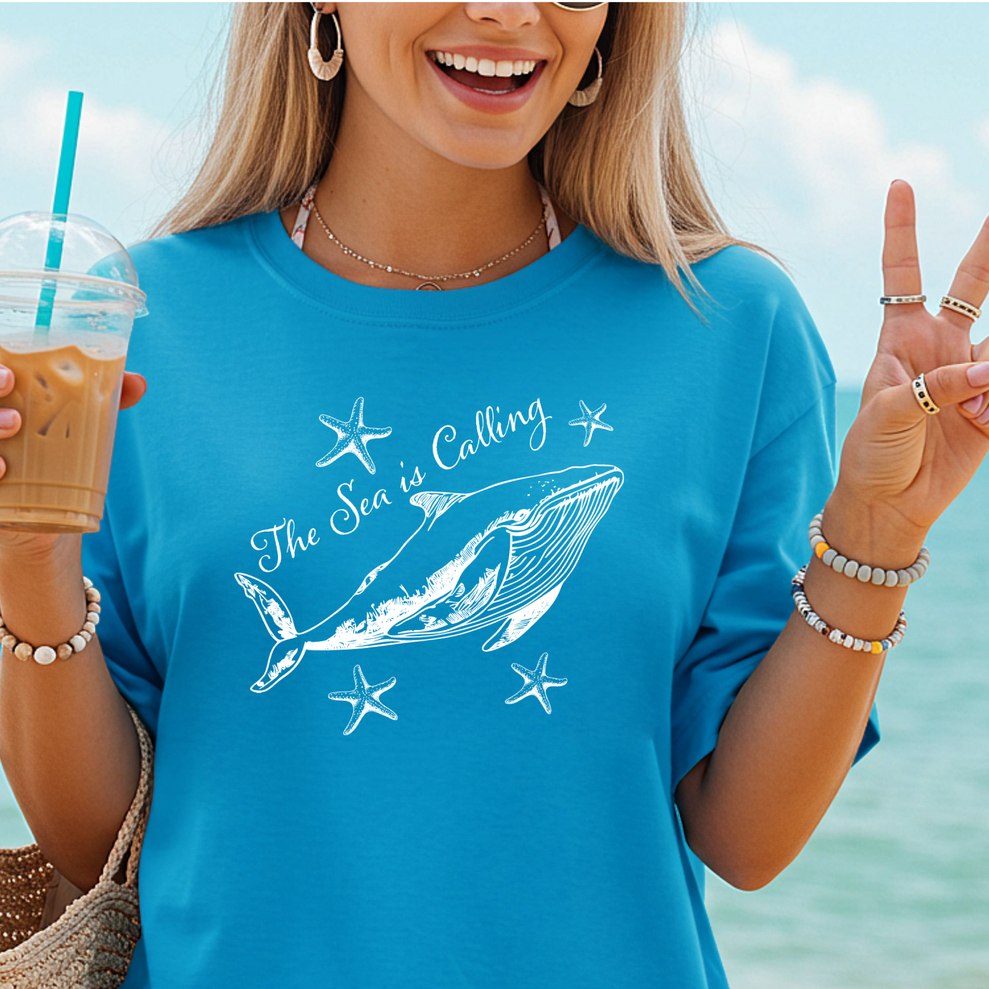 Comfort Colors t-shirt featuring a blue whale illustration surrounded by starfish and the handwritten-style text “The Sea is Calling.” The detailed marine artwork creates a calming coastal aesthetic. This unisex garment-dyed tee offers a soft vintage feel and relaxed fit, perfect for ocean lovers, beach trips, and anyone who enjoys sea-themed graphic shirts with a coastal vibe.
