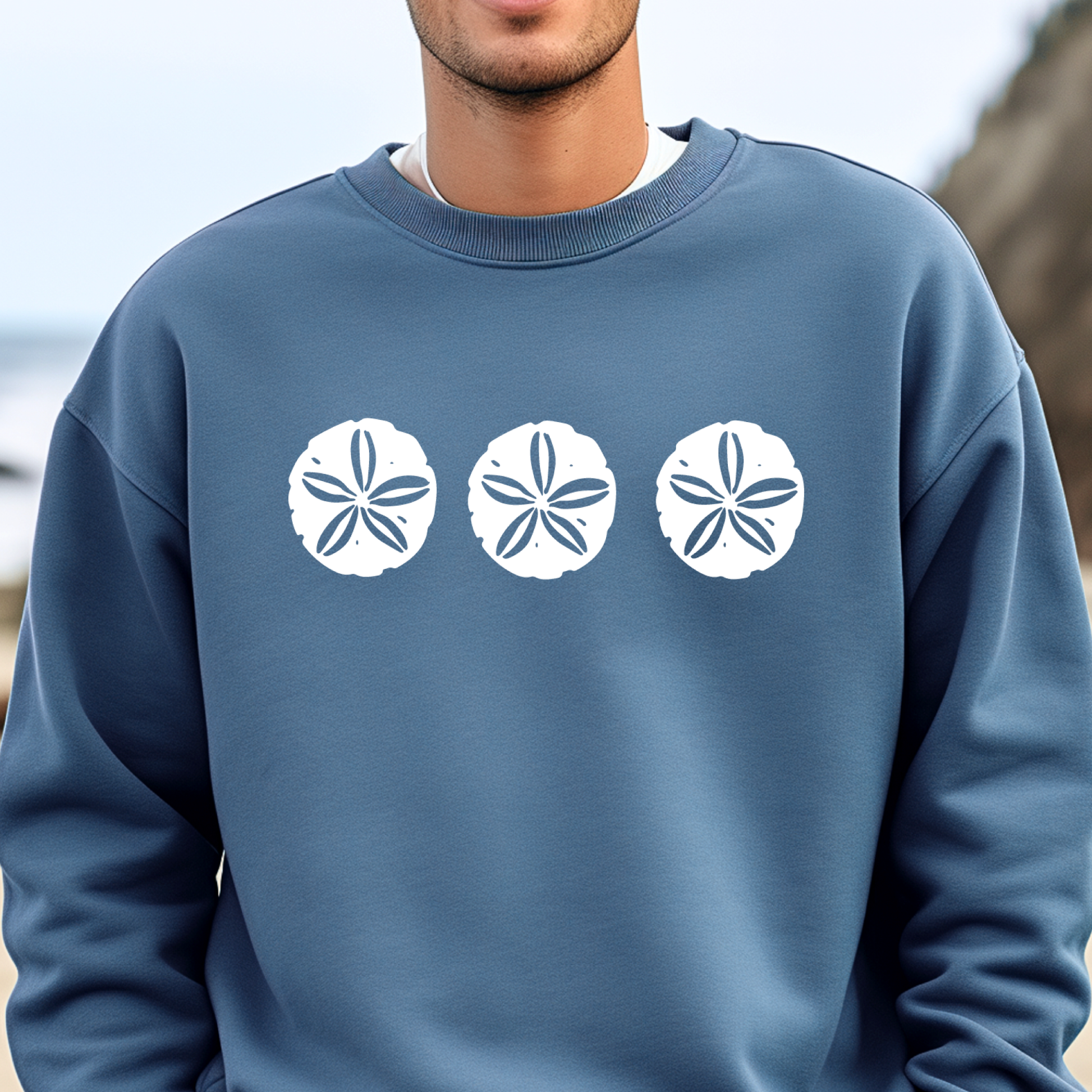 Gildan sweatshirt featuring three blue sand dollar graphics printed across the chest. Soft cotton-poly blend fabric with ribbed cuffs and waistband for a cozy, durable fit. Perfect for beach lovers and coastal style enthusiasts who appreciate simple ocean-inspired designs. Ideal for layering on cool seaside evenings or adding a subtle beach vibe to casual outfits.