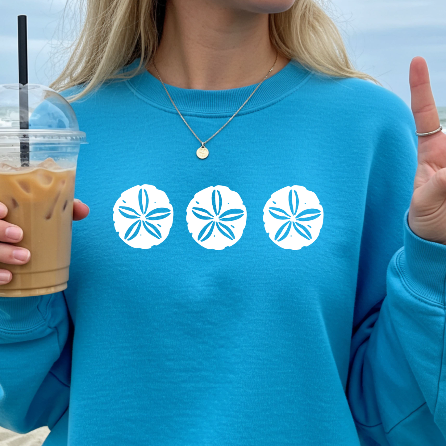 Gildan sweatshirt featuring three blue sand dollar graphics printed across the chest. Soft cotton-poly blend fabric with ribbed cuffs and waistband for a cozy, durable fit. Perfect for beach lovers and coastal style enthusiasts who appreciate simple ocean-inspired designs. Ideal for layering on cool seaside evenings or adding a subtle beach vibe to casual outfits.