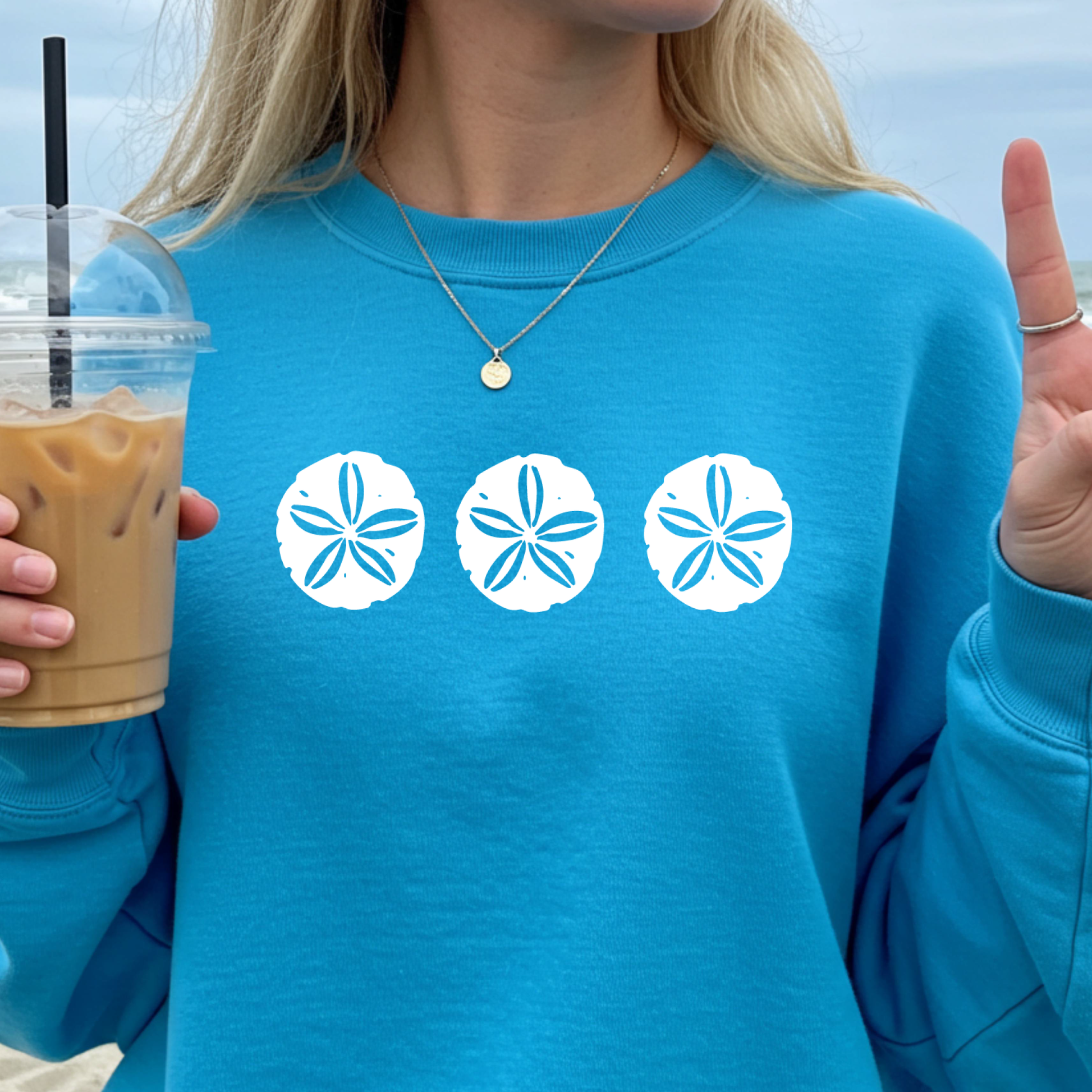 Gildan sweatshirt featuring three blue sand dollar graphics printed across the chest. Soft cotton-poly blend fabric with ribbed cuffs and waistband for a cozy, durable fit. Perfect for beach lovers and coastal style enthusiasts who appreciate simple ocean-inspired designs. Ideal for layering on cool seaside evenings or adding a subtle beach vibe to casual outfits.