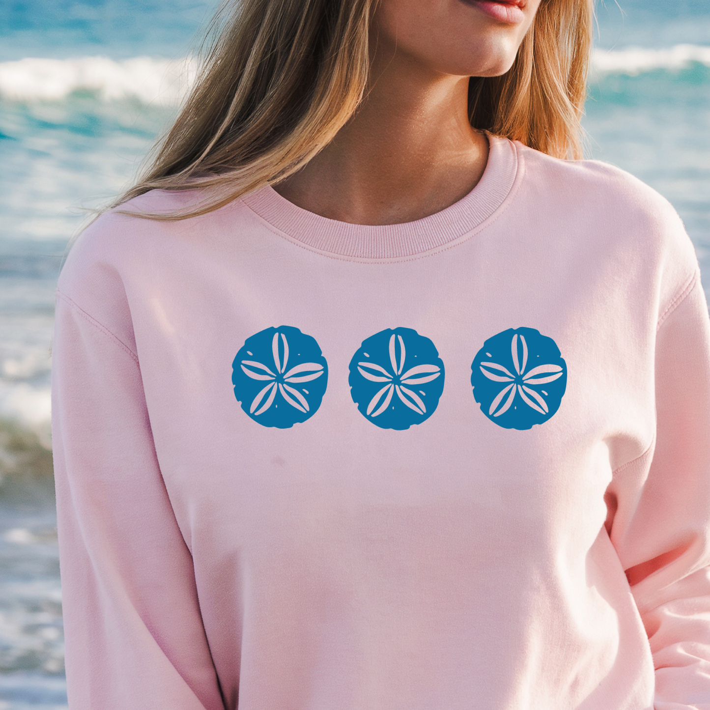 Gildan sweatshirt featuring three blue sand dollar graphics printed across the chest. Soft cotton-poly blend fabric with ribbed cuffs and waistband for a cozy, durable fit. Perfect for beach lovers and coastal style enthusiasts who appreciate simple ocean-inspired designs. Ideal for layering on cool seaside evenings or adding a subtle beach vibe to casual outfits.