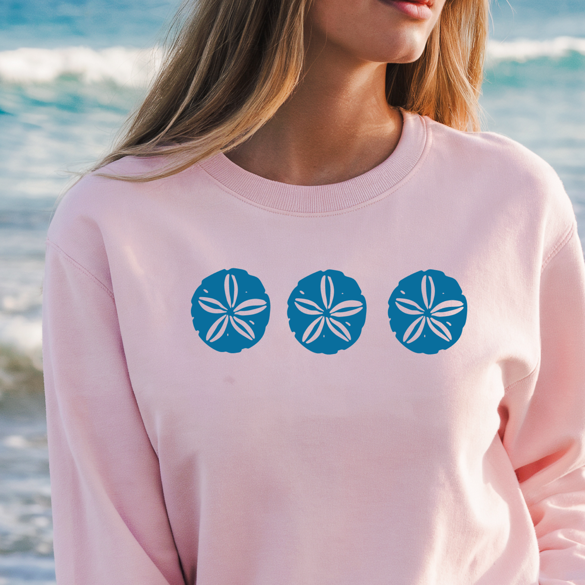 Gildan sweatshirt featuring three blue sand dollar graphics printed across the chest. Soft cotton-poly blend fabric with ribbed cuffs and waistband for a cozy, durable fit. Perfect for beach lovers and coastal style enthusiasts who appreciate simple ocean-inspired designs. Ideal for layering on cool seaside evenings or adding a subtle beach vibe to casual outfits.