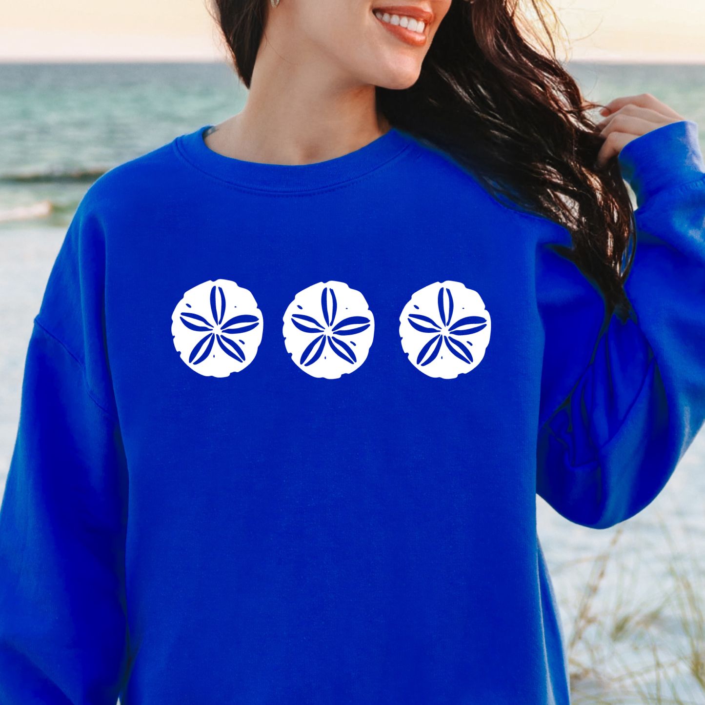 Gildan sweatshirt featuring three blue sand dollar graphics printed across the chest. Soft cotton-poly blend fabric with ribbed cuffs and waistband for a cozy, durable fit. Perfect for beach lovers and coastal style enthusiasts who appreciate simple ocean-inspired designs. Ideal for layering on cool seaside evenings or adding a subtle beach vibe to casual outfits.