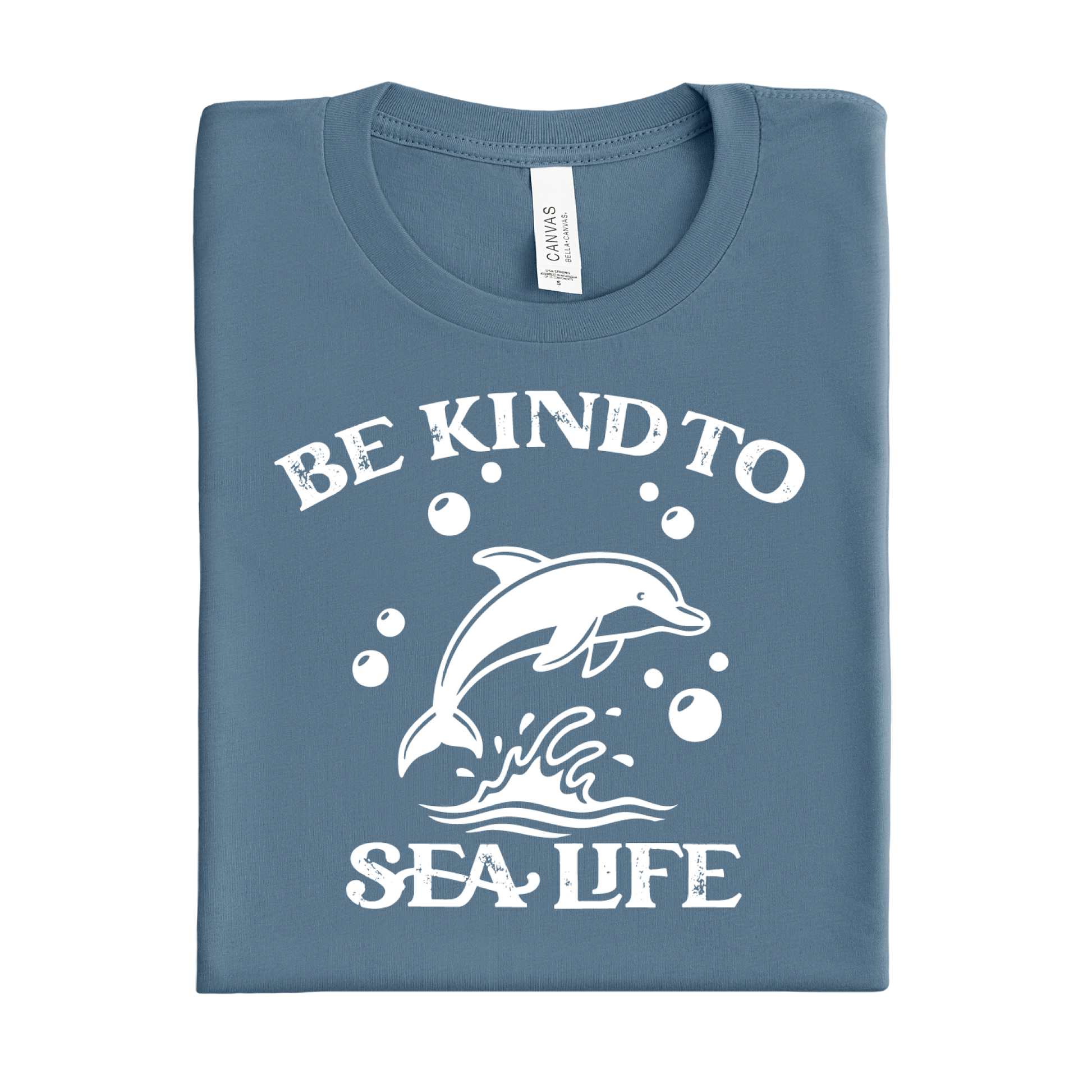 Folded steel blue t-shirt with a white dolphin graphic and text 'Be Kind to Sea Life' on a white background.