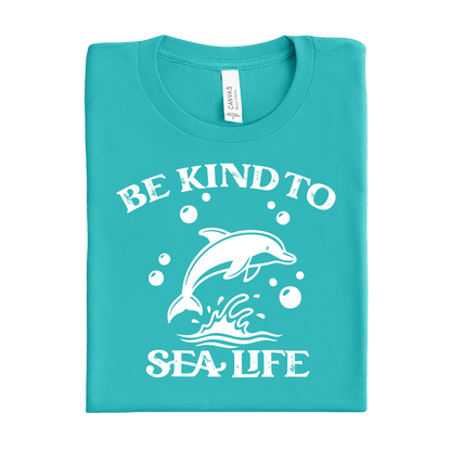 Folded teal t-shirt with white dolphin graphic and text 'Be Kind to Sea Life' on a white background