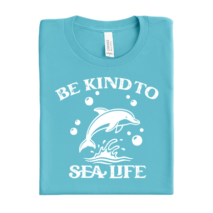 Folded turquoise t-shirt with white dolphin graphic and text 'Be Kind to Sea Life' on a white background
