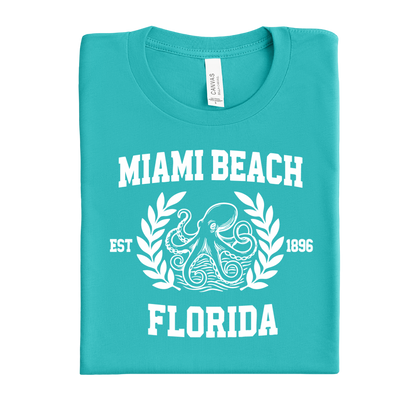 Folded teal t-shirt with 'Miami Beach, Florida' text and octopus design on a white background