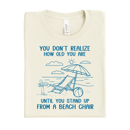 Natural t-shirt with blue beach-themed design and text on a white background