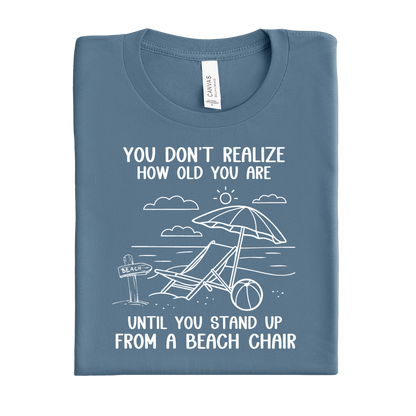 Folded blue steel t-shirt with beach graphic and text on a white background