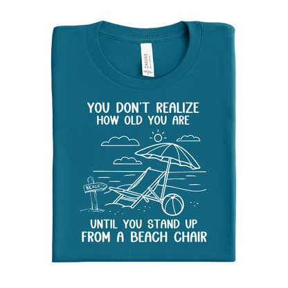 Folded deep teal t-shirt with beach-themed graphic and text on a white background