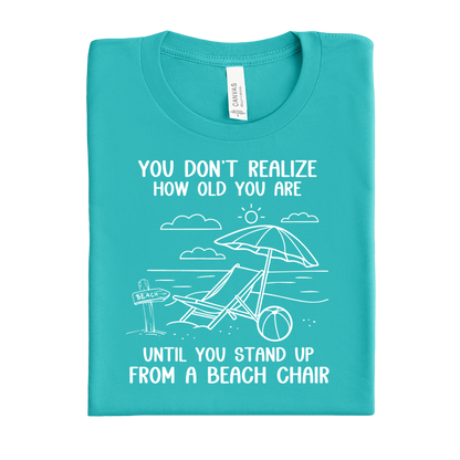 Folded teal t-shirt with beach-themed design and text on a white background