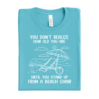 Folded turquoise t-shirt with beach graphic and text on a white background