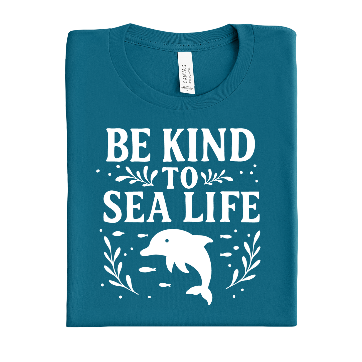 Folded deep teal t-shirt with 'Be Kind to Sea Life' text and dolphin graphic on a white background