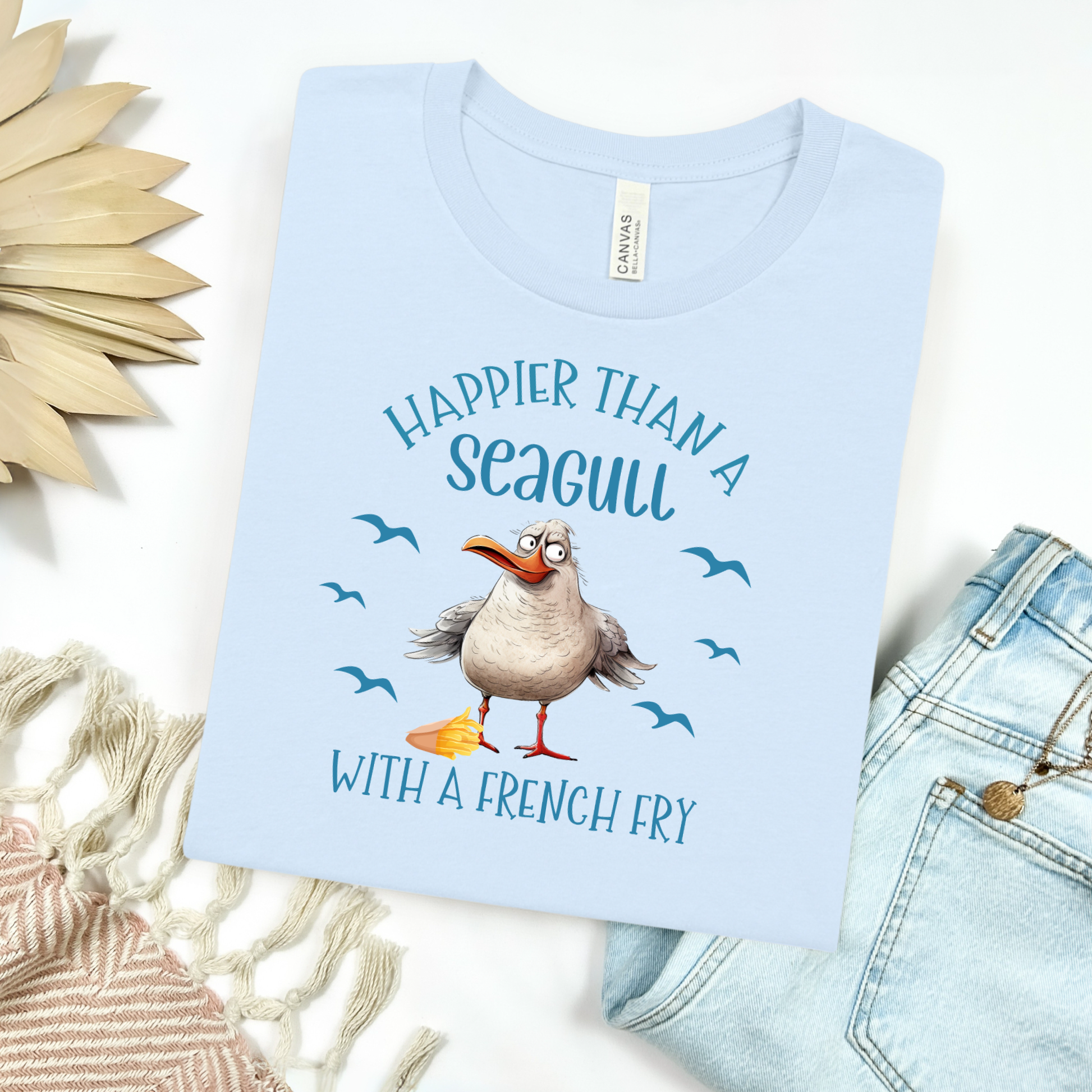 A Bella + Canvas t-shirt with a modern fit, super soft fabric, and lightweight feel—perfect for all-day comfort and casual coastal style. The front features a cute, chubby seagull graphic, standing proudly with a box of French fries by its foot, giving off cheeky beach-town energy. The seagull’s round shape and happy expression make it irresistibly fun.

Paired with the design is the playful text:
"Happier Than a Seagull with a French Fry"
