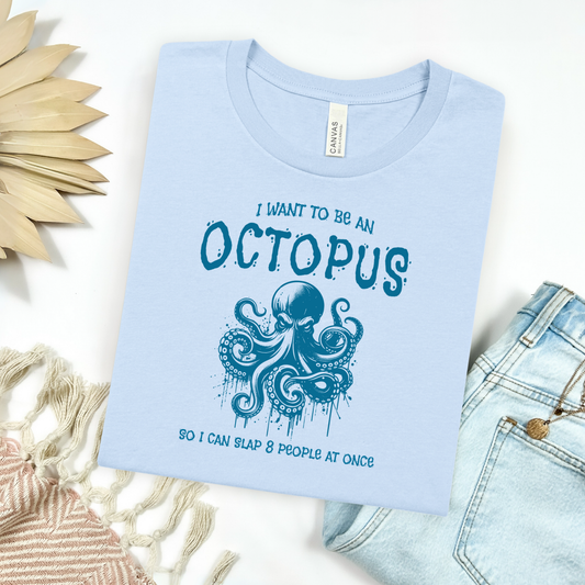 Bella Canvas 3001 "I Want To Be An Octopus So I Can Slap 8 People At Once" t shirt with an angry octopus one color graphic. Picture on a flay lay mockup with pair of blue jeans and blanket and a wicker sun shaped accessory.