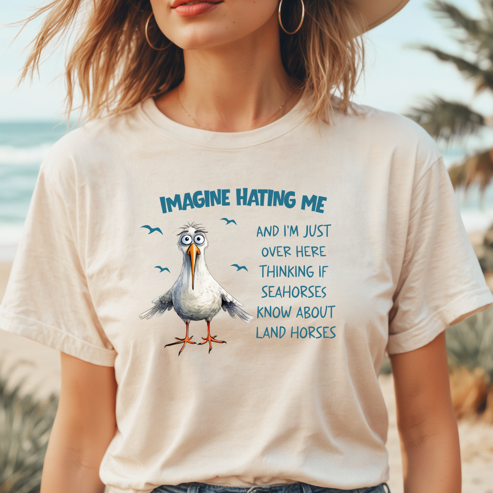 Person wearing a t-shirt with a cartoon seagull and humorous text on a beach.