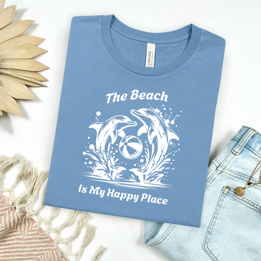 Bella Canvas 3001 "The beach is my happy place" t shirt of dolphins playing with a beach ball in one color graphic. Picture on a flay lay mockup with pair of blue jeans and blanket and a wicker sun shaped accessory.